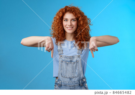 Charismatic sassy flirty redhead daring ginger girl curly haircut pointing down index fingers smiling broadly enthusiastic explore new store pointing promo like cool advertisement blue background Charismatic sassy flirty redhead daring ginger girl curly haircut pointing down index fingers smiling broadly enthusiastic explore new store pointing promo like cool advertisement blue background 84665482