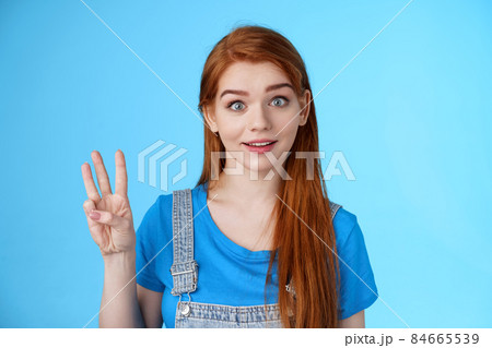Surprised cute redhead caucasian girl show number three, third, counting fingers, raise eyebrows ambushed, smiling curiously, stand blue background playful tender expression Surprised cute redhead caucasian girl show number three, third, counting fingers, raise eyebrows ambushed, smiling curiously, stand blue background playful tender expression 84665539