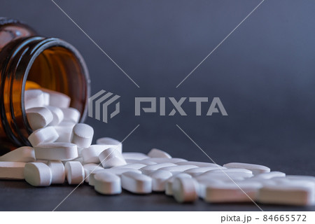 White large tablets falling out of the bottle. Medicine and treatment concept. 84665572