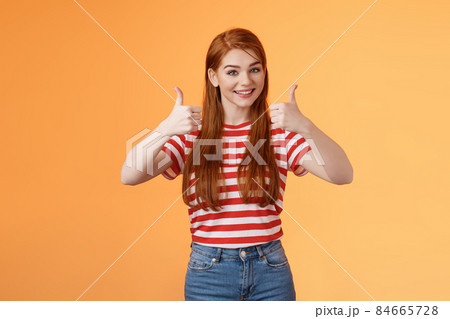 Good work, keep going. Girl encourage friend, say well done, show satisfactory sign, thumbs-up and smiling pleased, agree, approve nice choice, accept point view, stand orange background 84665728
