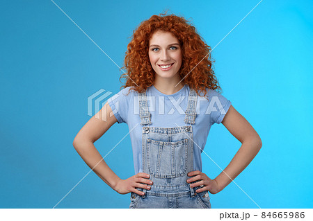Attractive sassy motivated redhead european female curly-haired hold hands waist empowered express confidence self-assured look forward ready win conqueror, stand blue background 84665986