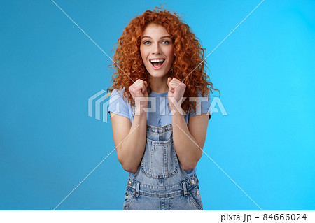Cheerful optimistic lucky redhead curly-haired attractive woman cheering clench fists joyfully smiling broadly cheering watching game supportive encourage keep up motivated blue background Cheerful optimistic lucky redhead curly-haired attractive woman cheering clench fists joyfully smiling broadly cheering watching game supportive encourage keep up motivated blue background 84666024