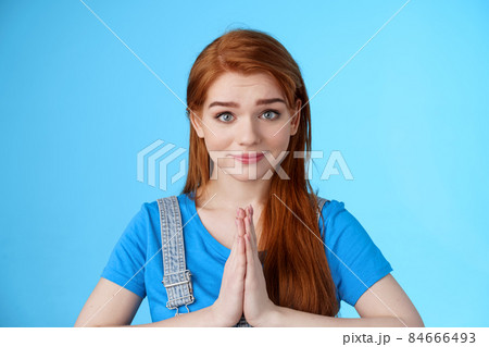Close-up attractive tender redhead woman asking pretty please, supplicating, hold hands pray, namaste gesture, look sincere pity, smiling begging help favor, stand blue background 84666493