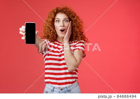 Amused impressed redhead good-looking curly-haired excited girl share awesome social media page show smartphone screen amazed touch cheek thrilled affected awesome app red background Amused impressed redhead good-looking curly-haired excited girl share awesome social media page show smartphone screen amazed touch cheek thrilled affected awesome app red background 84666494