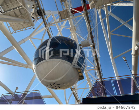 A large Ferris wheel against a blue sky. Booths with people go up 84667845