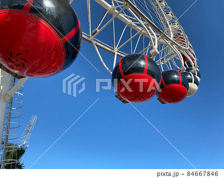 An Old Ferris Wheel With Bright Booths Against A Blue Sky 84667846