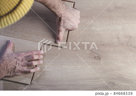 Installing laminate flooring in a room or office. Wooden parquet boards in the hands of a worker. Construction and decorative works for the finishing of housing Installing laminate flooring in a room or office. Wooden parquet boards in the hands of a worker. Construction and decorative works for the finishing of housing 84668339