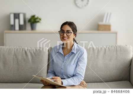Cheerful arab female psychologist writing in clipboard, having session with client, taking notes during consultation Cheerful arab female psychologist writing in clipboard, having session with client, taking notes during consultation 84668406