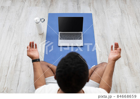 Millennial african american guy look at laptop with empty screen on mat on floor with bottle of water Millennial african american guy look at laptop with empty screen on mat on floor with bottle of water 84668659