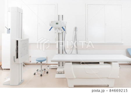 X-ray department in modern hospital. Radiology room with scan machine with empty bed. Technician adjusting an x-ray machine. Scanning chest, heart, lungs in modern clinic office. X-ray department in modern hospital. Radiology room with scan machine with empty bed. Technician adjusting an x-ray machine. Scanning chest, heart, lungs in modern clinic office. 84669215