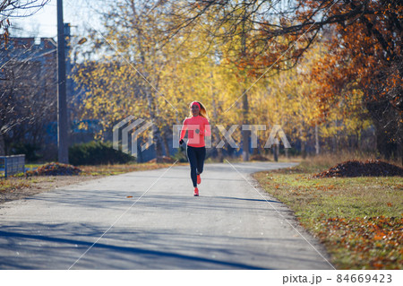 Young fitness woman running on the road in the cold morning in winter. 84669423