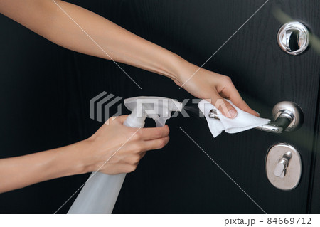 Cleaning black door handles with an antiseptic wet wipe and sanitizer spray. Disinfection in hospital and public spaces against corona virus. Woman hand using towel for cleaning home room door link. Cleaning black door handles with an antiseptic wet wipe and sanitizer spray. Disinfection in hospital and public spaces against corona virus. Woman hand using towel for cleaning home room door link. 84669712