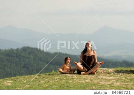 Mother in pose of lotus in mountains with little daughter. Mother in pose of lotus in mountains with little daughter. 84669721