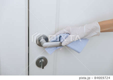 Cleaning door handle with blue wipe in white gloves. Sanitize surfaces prevention in hospital and public spaces against corona virus. Woman hand using towel for cleaning home room door link. Cleaning door handle with blue wipe in white gloves. Sanitize surfaces prevention in hospital and public spaces against corona virus. Woman hand using towel for cleaning home room door link. 84669724
