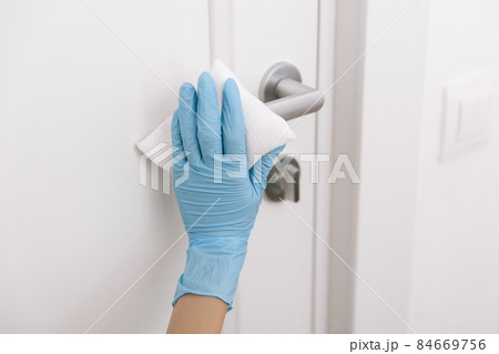 Cleaning black door handles with an antiseptic wet wipe and blue gloves. Sanitize surfaces prevention in hospital and public spaces against corona virus. Woman hand using towel for cleaning. 84669756