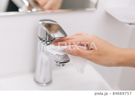 Cleaning the sink faucet with a microfiber cloth. Sanitize surfaces prevention in hospital and public spaces against corona virus. Woman hand using wet wipe. Cleaning the bathroom. 84669757