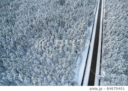 Aerial view of asphalt highway leading through frosty winter forests and groves covered with hoarfrost and snow. Drone photo of black road line and trees with chill snow in mountains. Christmas theme Aerial view of asphalt highway leading through frosty winter forests and groves covered with hoarfrost and snow. Drone photo of black road line and trees with chill snow in mountains. Christmas theme 84670401
