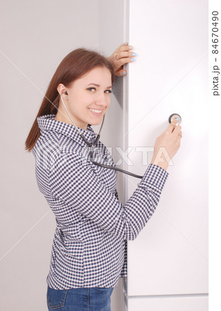 Young woman listening closed fridge with stethoscope Young woman listening closed fridge with stethoscope 84670490