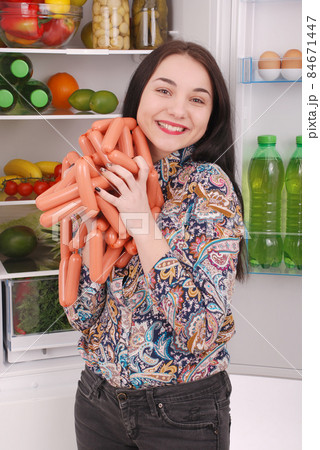 Young girl holds sausages on the refrigerator background Young girl holds sausages on the refrigerator background 84671447