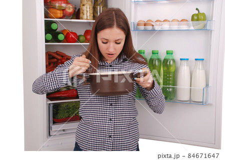 Beautiful Woman Tasting food on the refrigerator background Beautiful Woman Tasting food on the refrigerator background 84671647