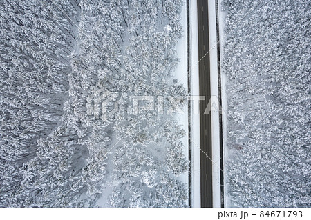 Aerial view of asphalt highway leading through frosty winter forests and groves covered with hoarfrost and snow. Drone photo of black road line and trees with chill snow in mountains. Christmas theme 84671793