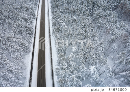 Aerial view of asphalt highway leading through frosty winter forests and groves covered with hoarfrost and snow. Drone photo of black road line and trees with chill snow in mountains. Christmas theme 84671800