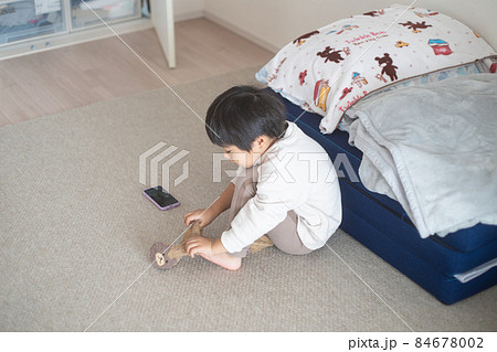 日当たりの良い部屋でスマホで会話しながら靴下を履く4歳児 84678002