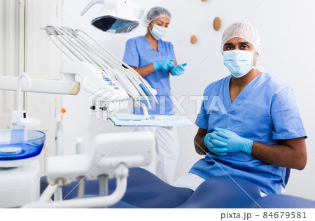 Qualified dentist standing in blue uniform in dental office Qualified dentist standing in blue uniform in dental office 84679581
