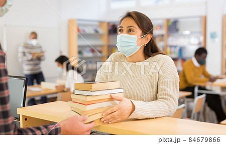 Woman in mask returning books at library 84679866