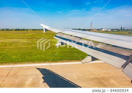View of airplane wing, blue skies and green land with plane shadow during landing. Airplane window view. 84680934