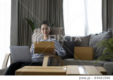 Happy asian woman opening cardboard box or parcel in living room. Happy asian woman opening cardboard box or parcel in living room. 84681996