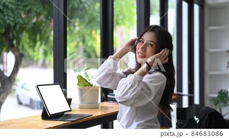 Cheerful young woman wearing wireless headphone and using computer tablet. 84683086