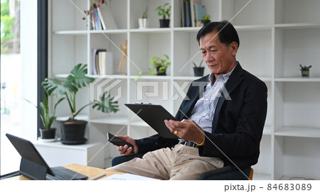 Mature businessman working with computer tablet and analyzing financial reports in office. 84683089