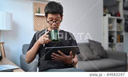 Young man drinking coffee and checking news on digital table at home. 84683297