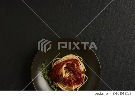 pasta concept a dish of boiled long slim pasta with red sauce being served on the black table together with a wooden spoon and fork 84684812