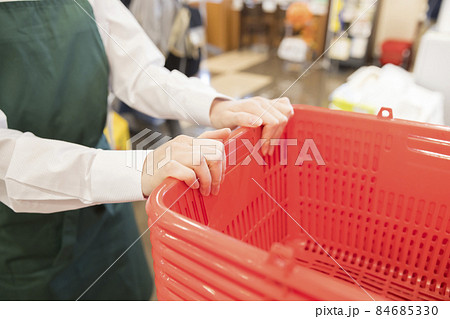 スーパーで清算済み用の買い物かごを移動する女性従業員手元 84685330