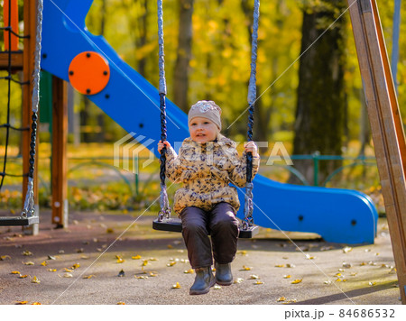 Baby girl sitting on a swing on a playground in an autumn park. 84686532