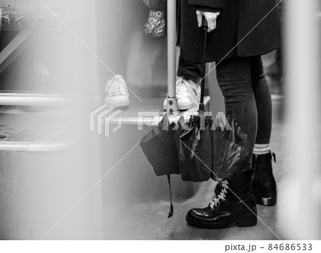 Selective focus on an umbrella at the feet of a girl standing in the cabin of a city bus. Black and white image. 84686533