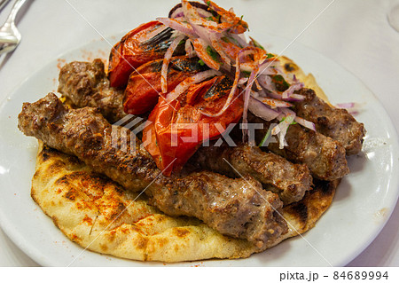 Greek souvlaki kebap with grilled tomatoes, on a pita bread. 84689994