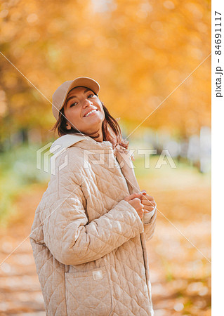 Fall concept - beautiful woman drinking coffee in autumn park under fall foliage 84691117