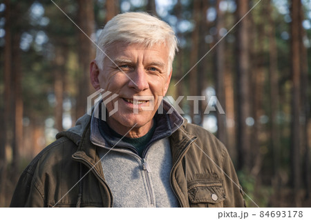 Old man wearing warm clothes enjoying walking at the forest near the trees 84693178