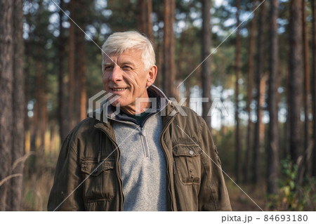 Mature male person standing at the forest around the trees and smiling toothy 84693180
