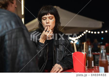 Relaxed female person sitting at the cafe with her boyfriend and smoking cigarette Relaxed female person sitting at the cafe with her boyfriend and smoking cigarette 84694488