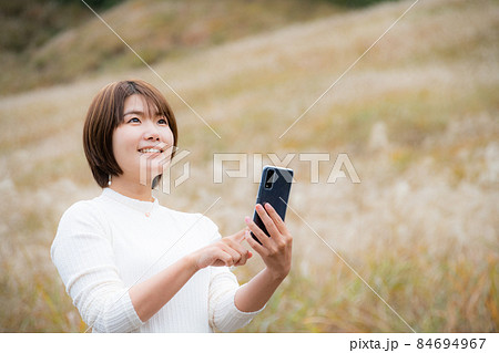 秋の風景の中にいるスマートフォンを持った女性 秋の風景の中にいるスマートフォンを持った女性 84694967
