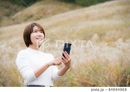 秋の風景の中にいるスマートフォンを持った女性 秋の風景の中にいるスマートフォンを持った女性 84694968