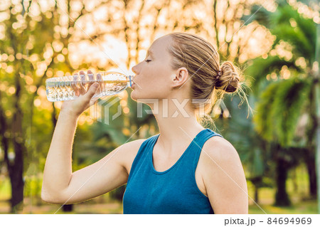 Attractive sporty woman drinking water from a bottle after jogging or running Attractive sporty woman drinking water from a bottle after jogging or running 84694969