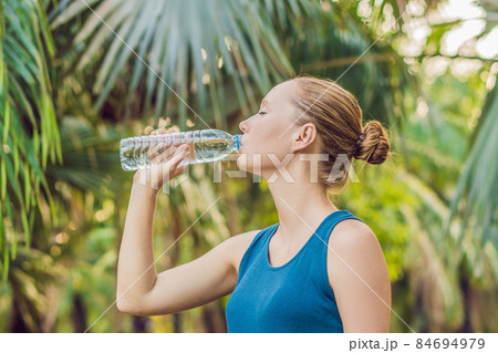 Attractive sporty woman drinking water from a bottle after jogging or running Attractive sporty woman drinking water from a bottle after jogging or running 84694979