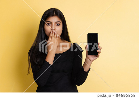 Young beautiful girl, student in black blouse closing mouth with her hand palm isolated on yellow color studio background 84695858