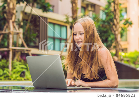 Young female freelancer sitting near the pool with her laptop in the hotel browsing in her smartphone. Busy at holidays. Distant work concept. Copy space for your text Young female freelancer sitting near the pool with her laptop in the hotel browsing in her smartphone. Busy at holidays. Distant work concept. Copy space for your text 84695923