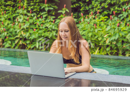 Young female freelancer sitting near the pool with her laptop in the hotel browsing in her smartphone. Busy at holidays. Distant work concept. Copy space for your text Young female freelancer sitting near the pool with her laptop in the hotel browsing in her smartphone. Busy at holidays. Distant work concept. Copy space for your text 84695929